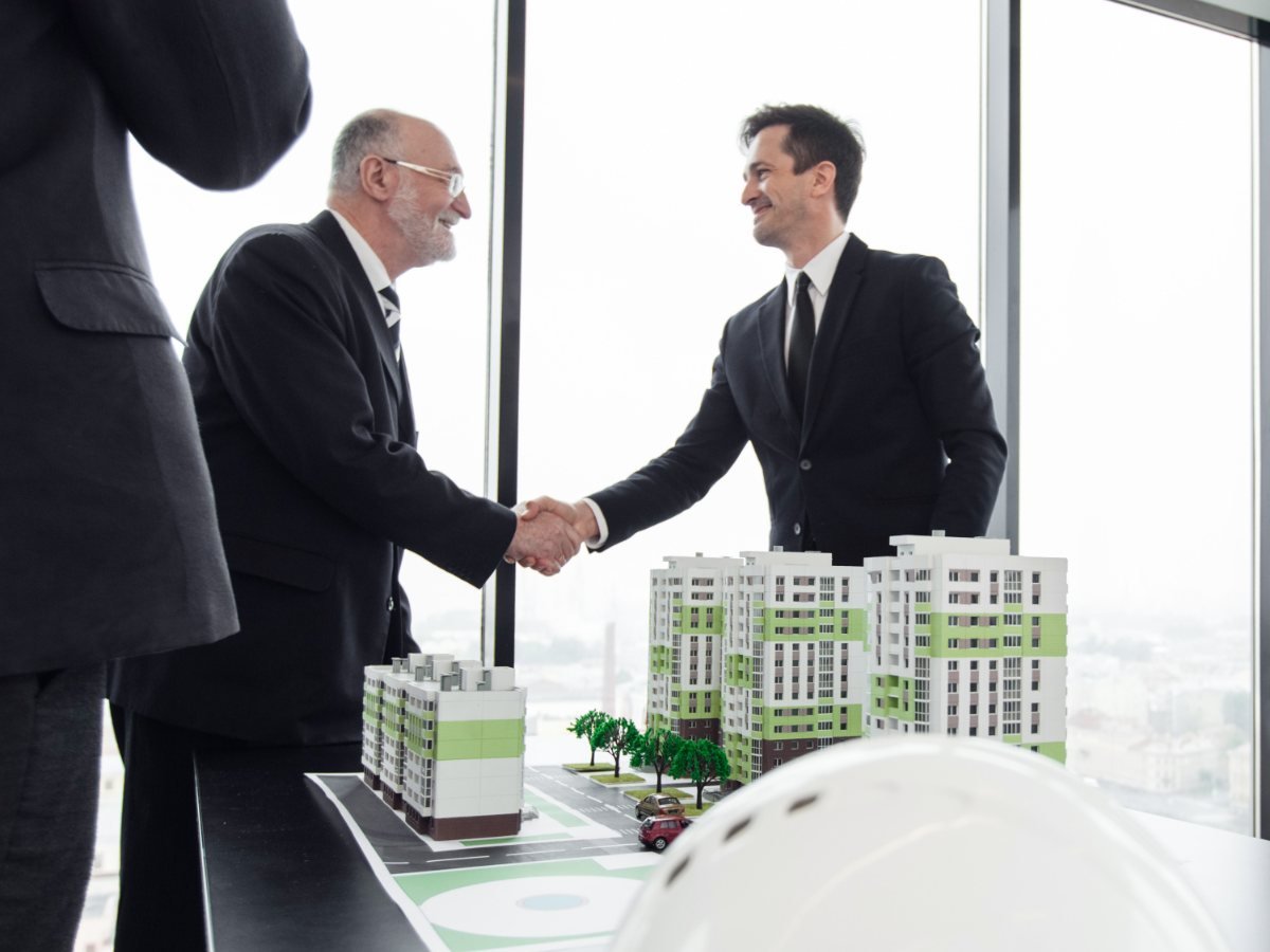 Landowner and developer shaking hands over a model of a housing project